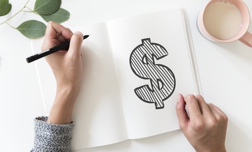 person's-hands-holding-pen-near-notebook-with-large-dollar-sign-drawn-inside