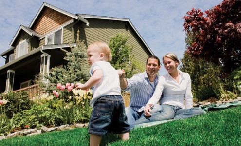 toddler-on-grassy-hill-with-parents-and-house-in-background