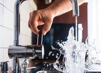 person-holding-faucet-handle-while-water-splashes-in-overflowing-glass