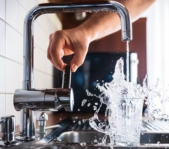 person-holding-faucet-handle-while-water-splashes-in-overflowing-glass