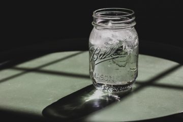 ball mason jar with ice water sitting on surface with sunlight coming through window