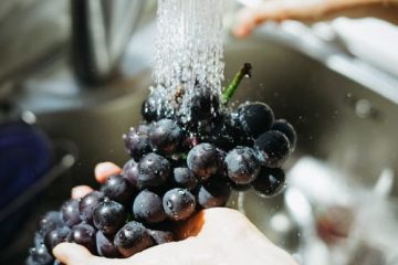 hands-holding-purple-grapes-under-stream-of-water-from-sink-faucet