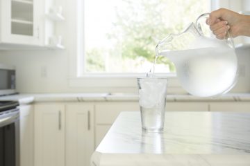 clear-pitcher-pouring-water-into-glass-on-kitchen-counter
