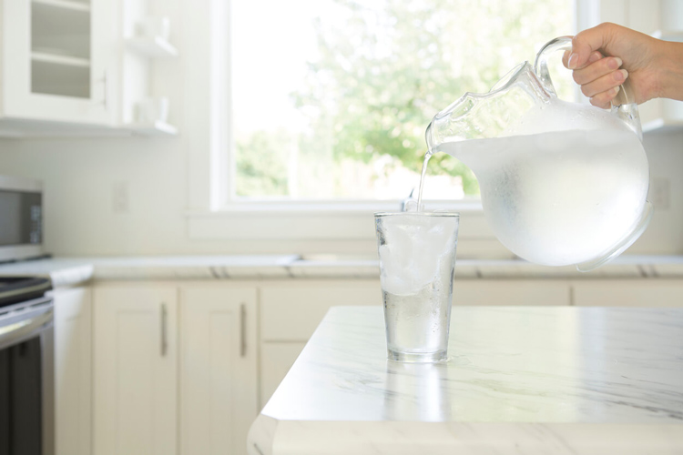 clear-pitcher-pouring-water-into-glass-on-kitchen-counter