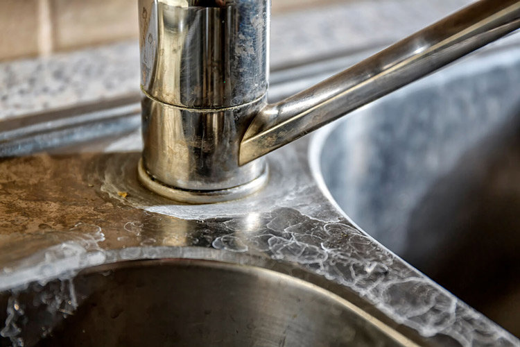 Close-up of a kitchen tap and sink with hard water calcification