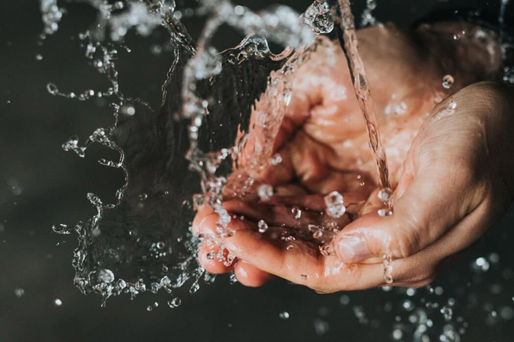 hands-cupping-water-splashing-from-faucet-with-dark-background