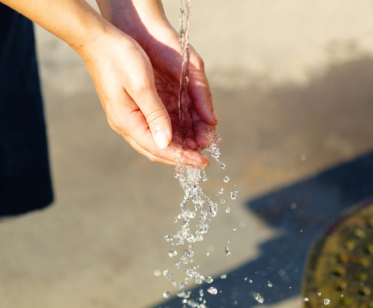 person-cupping-hands-to-catch-stream-of-falling-water-outside