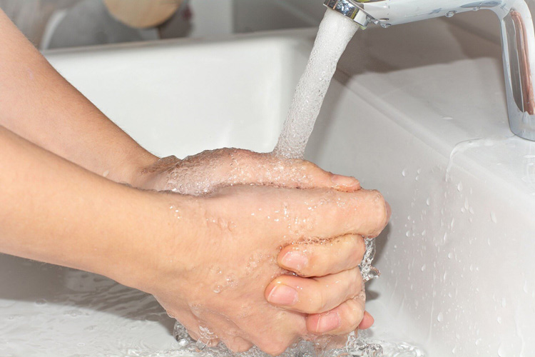 clasped-hands-under-running-hard-water-from-faucet-at-white-sink
