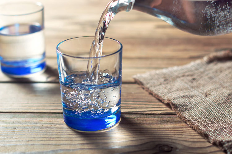 pitcher-pouring-water-into-glass-on-wooden-table-with-second-water-glass-in-background