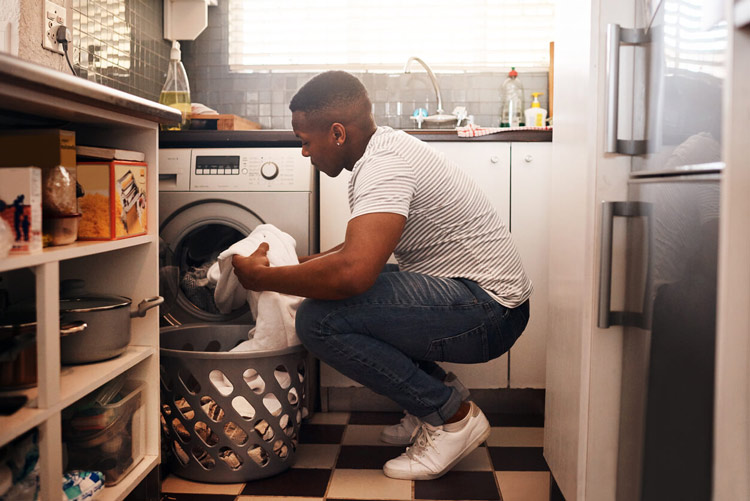 young-man-crouching-by-washing-machine-looking-at-hard-water-stain-on-white-shirt