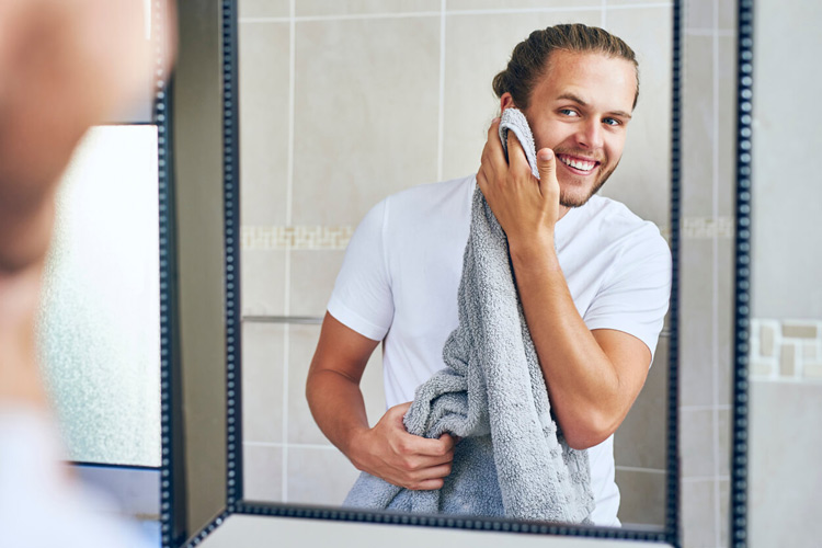 young-man-smiling-while-drying-face-with-towel-in-bathroom