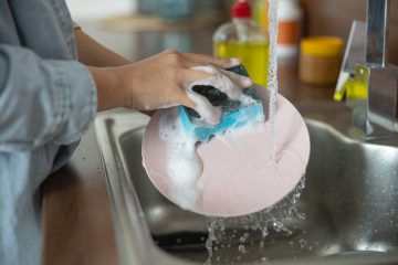 close-up-of-person's-hands-washing-pink-plate-with-soapy-sponge-under-running-water-in-sink