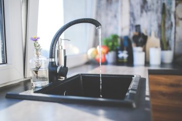 A black sink and faucet in a kitchen with a sunny window and items at the end of the counter