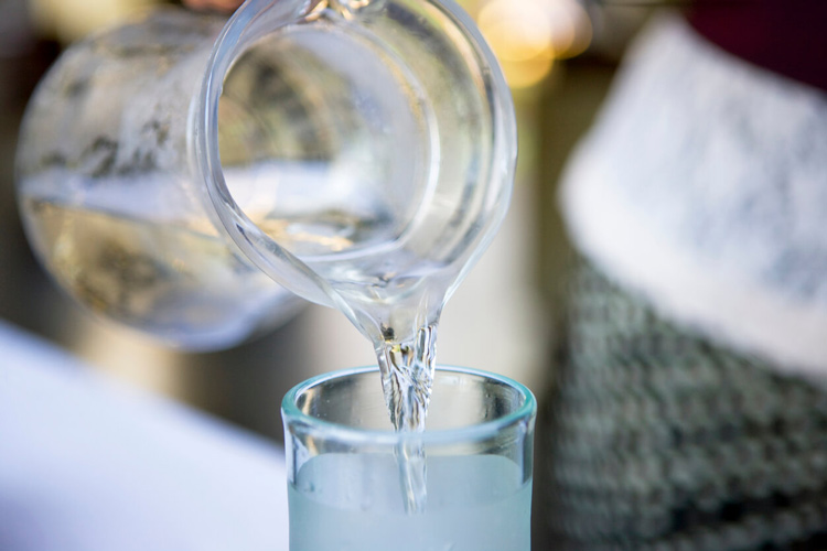 A glass pitcher pouring water into a tall glass.