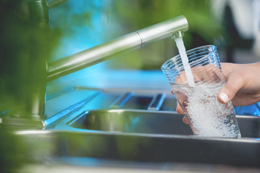 A hand holding a glass under a running water faucet at a kitchen sink