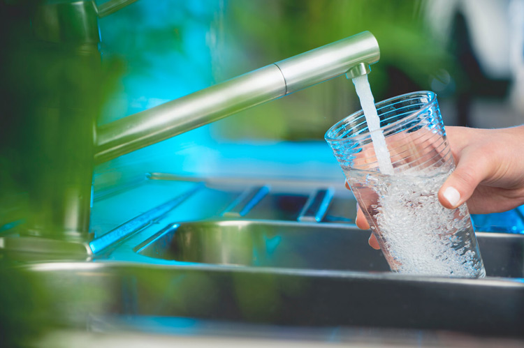 A hand holding a glass under a running water faucet at a kitchen sink