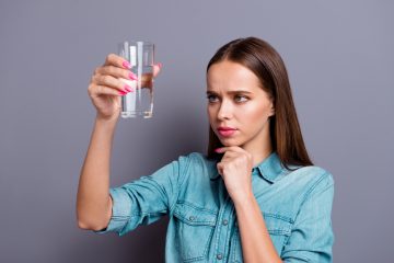 A woman holding up a glass of water to check its quality and cleanliness