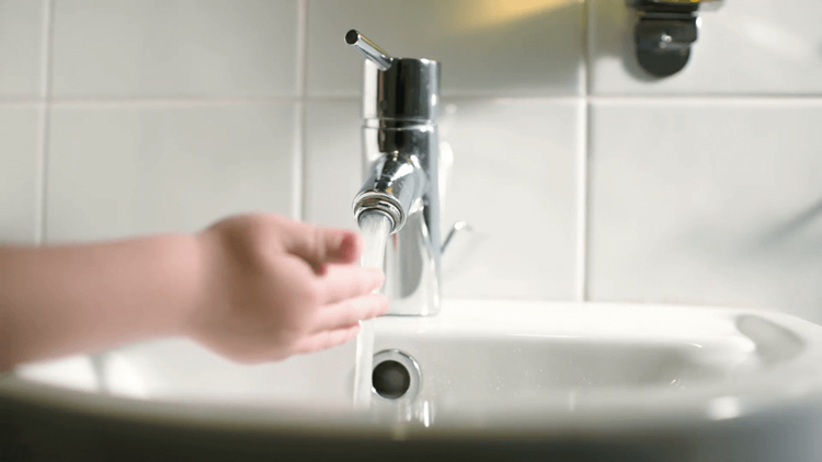 Childs-hand-touching-carefully-water-stream-pouring-from-tap-in-the-bathroom_qkwmr0wyr